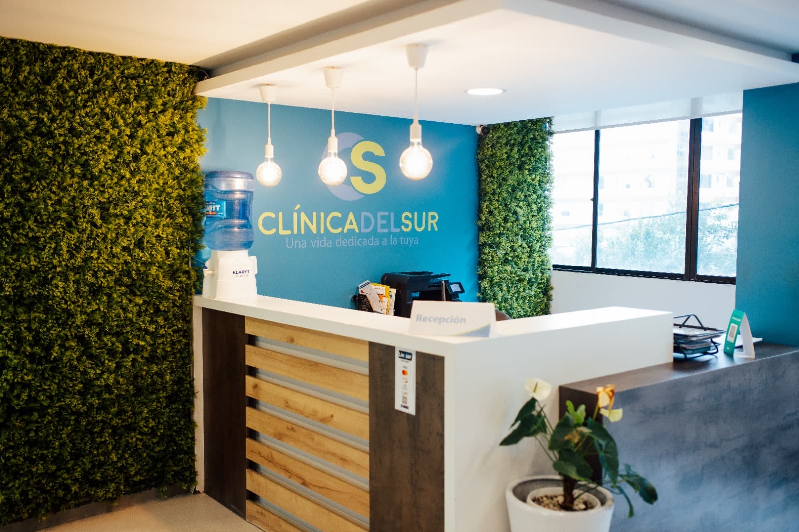 Mostrador de recepción con muro vegetal y el logotipo de la clínica iluminado